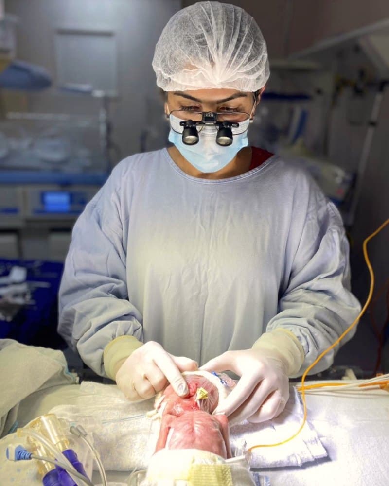 Dra. Karimy Mehanna em cirurgia neonatal, com lupas cirúrgicas, em unidade de terapia intensiva